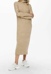 Abito a dolcevita beige in maglia a costine, di lunghezza al ginocchio, abbinato a scarpe da ginnastica bianche, con maniche lunghe e una silhouette rilassata.