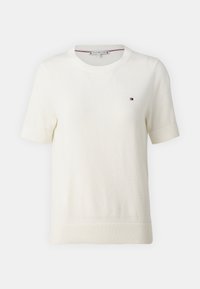 Krátký rukáv, svetr v krémové barvě s kulatým výstřihem. Součástí je malé logo na levé straně hrudi a žebrované manžety a lem. Měkká textura.