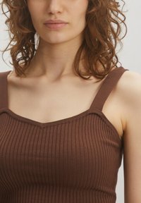 Brown ribbed tank top with wide shoulder straps and a V-shaped neckline. The fabric is textured, emphasizing a fitted design.