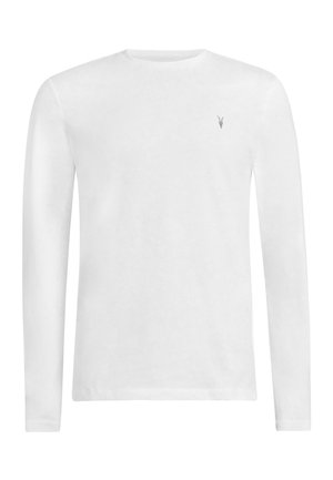 Camisa blanca de manga larga, pantalones de mezclilla gris con un ligero desgaste, cinturón negro con acentos circulares, gafas de sol negras y una bolsa negra.