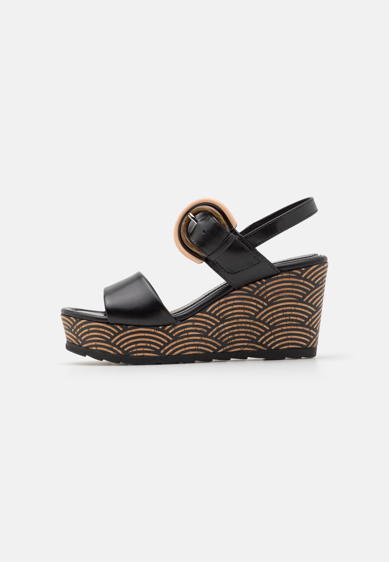 Black wedge sandal with a glossy finish, featuring a round tan buckle and a textured brown outsole with a wave pattern.