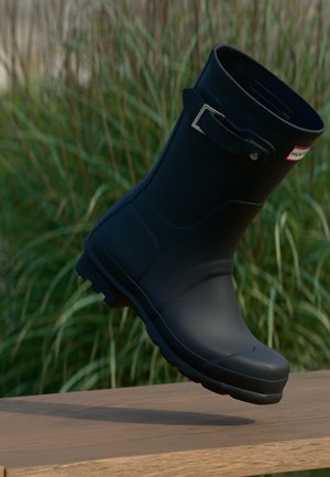 Botte de pluie en caoutchouc noir avec un petit talon, un bout arrondi et un accent en boucle en argent. Présente une semelle texturée pour une meilleure adhérence.