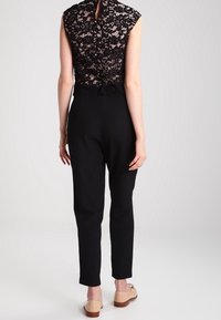 Top de encaje negro con mangas cortas, combinado con pantalones negros de cintura alta. Detalles notables incluyen un ojal en la parte posterior y una cintura ajustada.