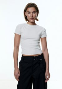 Witte geribbelde korte mouw crop top met een geschulpte halslijn, gecombineerd met zwarte hooglopende cargobroek met een ringriemaccent.