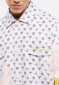 Witte shirt met patroon grafische ontwerpen in bruin, met een omklapbare kraag, twee borstzakken en een label met "CARLO COLUCCI" in goud.