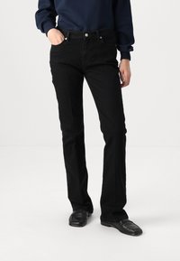 Black denim jeans with a slim fit, five-pocket design, white stitching, and silver button accents, worn with a navy sweatshirt.