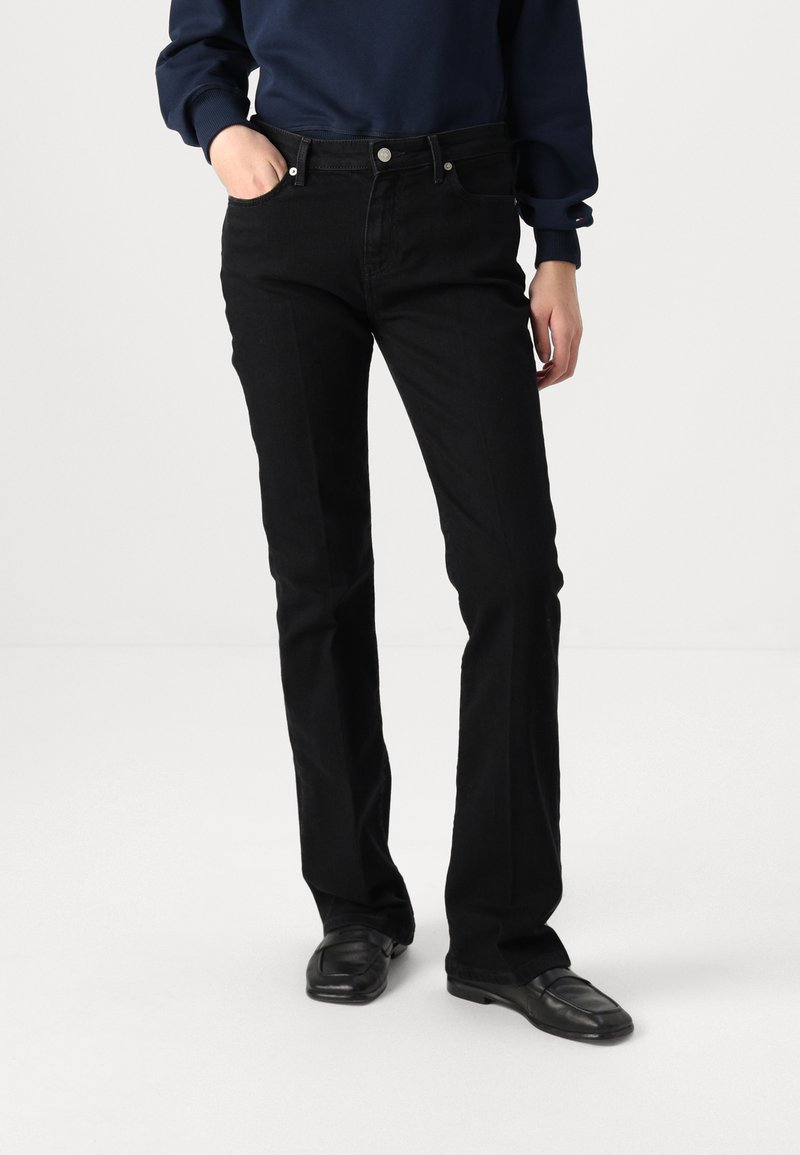 Black denim jeans with a slim fit, five-pocket design, white stitching, and silver button accents, worn with a navy sweatshirt.
