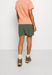 Camiseta de manga corta melocotón y falda verde, con tejido suave y un corte relajado. Se lleva con calcetines grises y zapatos de senderismo marrones.