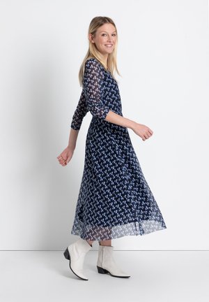 Navyblaues Midikleid mit durchsichtigen, gemusterten langen Ärmeln und einem fließenden Rock; kombiniert mit weißen Ankle-Boots. Verfügt über eine taillierte Taille.