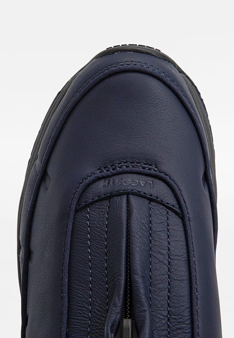 Zapato de piel azul marino con puntera redondeada, detalles de costura y logotipo "Lacoste" en relieve en el empeine.