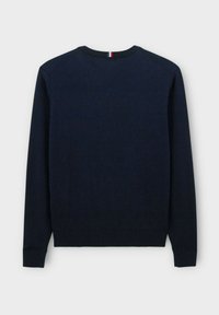 Pull marin bleu, col ras du cou, avec des poignets et un ourlet côtelés, en tissu tricoté texturé, arborant une petite étiquette rouge, blanche et bleue au niveau du col.
