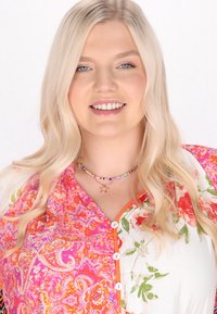 Top con motivo floreale realizzato in tessuto rosa e bianco, con scollatura rotonda e dettagli con bottoni arancioni. Indossato con una collana di perle.