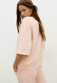 Helle rosa, oversized Sweatshirt aus Fleece mit Rundhalsausschnitt, fallenden Schultern und umgeschlagenen Bündchen, kombiniert mit passenden Hosen.
