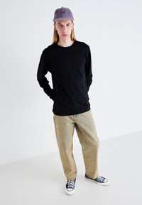 Black long-sleeve t-shirt, light beige loose-fit jeans, blue sneakers with white soles, and a light purple cord cap. Minimalist design.