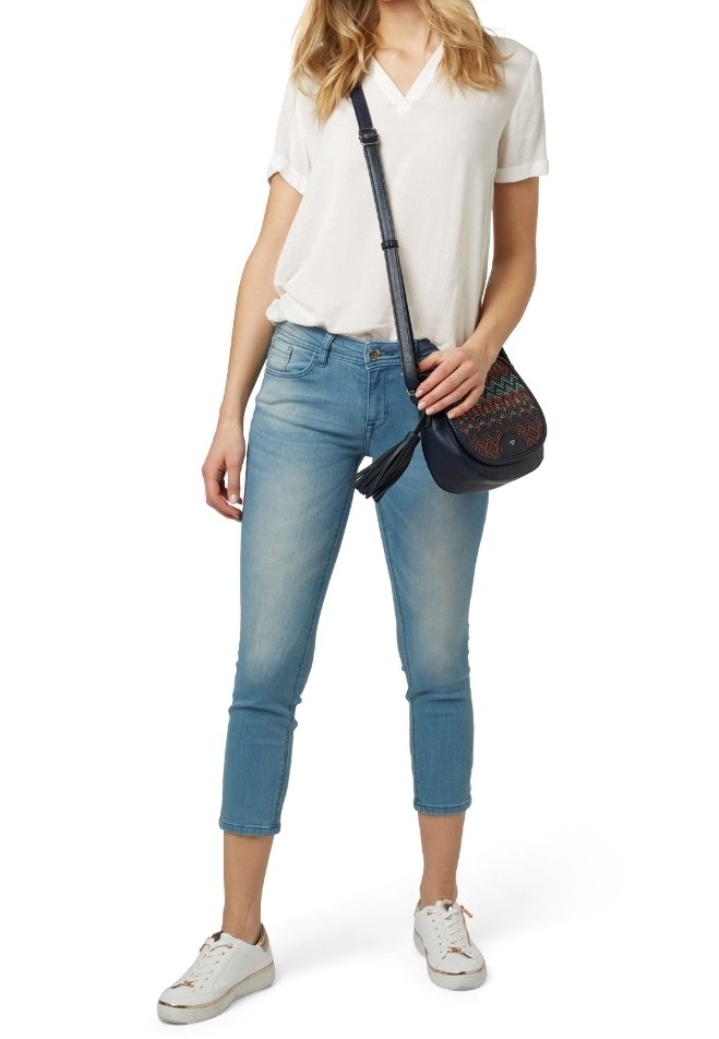 T-shirt blanc léger à col en V, jean bleu clair retroussé et baskets blanches. Un petit sac bandoulière noir avec broderies colorées et pompon.