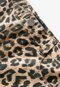 Tejido de estampado de leopardo, base beige con manchas verdes oscuras, con un botón metálico y costuras visibles, que enfatizan un estilo de denim casual.