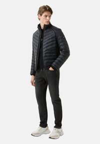 Czarna pikowana kurtka puchowa z wysokim kołnierzem, zamkiem z przodu i bocznymi kieszeniami, w połączeniu z ciemnymi dżinsami i białymi trampkami.