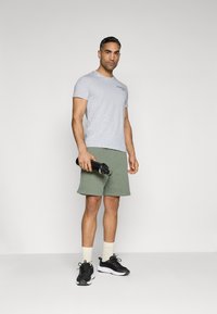 Grey short-sleeve t-shirt, olive green shorts, black sneakers, holding a black water bottle. Simple design, fabric texture visible.