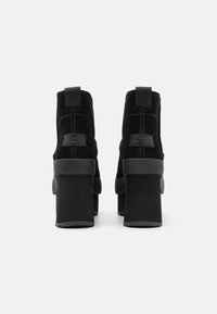 Bottines en daim noir à talon bloc épais, dotées d'une languette de tirage et de détails de surpiqûres discrètes. Design élégant avec une finition texturée.