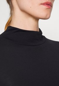 Top nero a collo alto realizzato in tessuto liscio e elastico, con un design aderente e cuciture minime per un aspetto elegante.