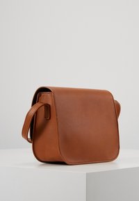 Brązowa skórzana torba na ramię o miękkiej fakturze, prostokątnym kształcie, pojedynczym pasku na ramię oraz zamknięciu na klapę.