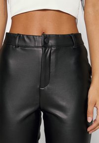 Black faux leather pants with a smooth texture, high waist, a front zipper, and a metal snap closure. Features slim-fit design with no visible patterns.