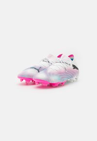 Scarpe da calcio bianche con accenti rosa, una tomaia testurizzata con motivi a gradiente e un design dinamico, dotate di tacchetti.
