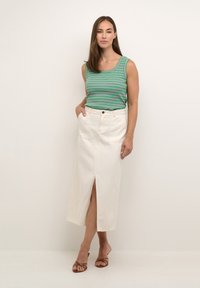 Gestreiftes grünes Tanktop mit pinken Streifen; weiße Denim-Midi-Rock mit vorderem Schlitz und Taschen. Braune Riemchensandalen. Neutrale Hintergrund.