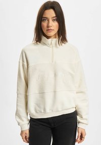 Weißes Sweatshirt mit halbem Reißverschluss, aus texturiertem Stoff über der Brust und einem gestickten Akzent mit der Aufschrift "Definitiv." Lässiger Schnitt.