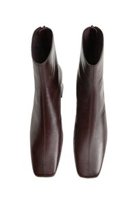 Un par de botas de piel marrón oscuro hasta el tobillo con punteras cuadradas y cremalleras laterales, vistas desde arriba sobre un fondo blanco.