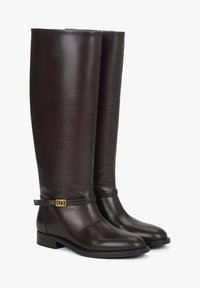 Brązowe, skórzane kozaki sięgające kolan o smukłym kroju, płaskiej podeszwie i złotym akcentem na pasku przy kostce. Gładka faktura, minimalne zdobienia.