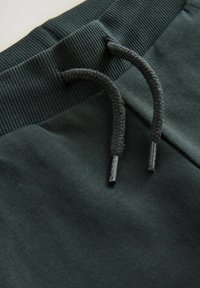 Donkergroene sweatpants hebben een geribde tailleband met een trekkoord, textielstof en platte naden bij de taille voor een nette afwerking.
