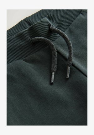 Dunkelgrüne Sweatpants verfügen über einen gerippten Bund mit einem Kordelzug, strukturierter Stoff und flache Nähte in der Taille für einen sauberen Abschluss.