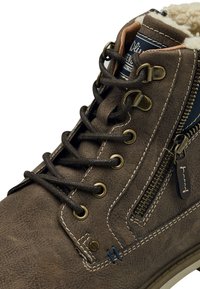 Botín de cuero marrón que presenta ojales de metal, cordones, una cremallera lateral, costuras en contraste y un forro interior suave.