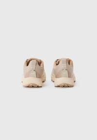 Beige joggesko med en teksturert stoffoverdel, kontrasterende mesh-paneler og såle av formet gummi, med en løpesnor på hælen.