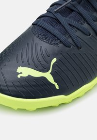 Dark blue synthetic soccer shoe with textured surface, lime green accents, and distinctive Puma logo. Features lace-up closure and sculpted outsole.