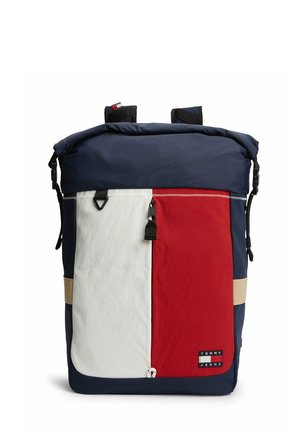 Marineblå rygsæk med frontlomme i hvid og rød, sort lynlås og "Tommy Jeans" logo patch nederst i højre hjørne.