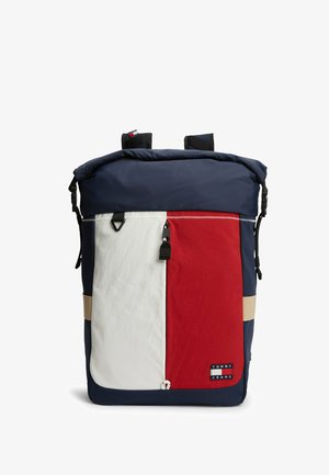 Marineblå rygsæk med frontlomme i hvid og rød, sort lynlås og "Tommy Jeans" logo patch nederst i højre hjørne.