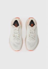 Witte sportieve schoenen met een gestructureerde bovenkant, een mesh-ontwerp en feloranje accenten. Voorzien van grijze veters en een gewatteerde zool.