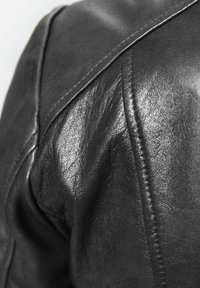 Schwarze Lederjacke mit einer Nahaufnahme der Schulternaht, die das strukturierte Material und die sichtbaren Nähdetails zeigt.