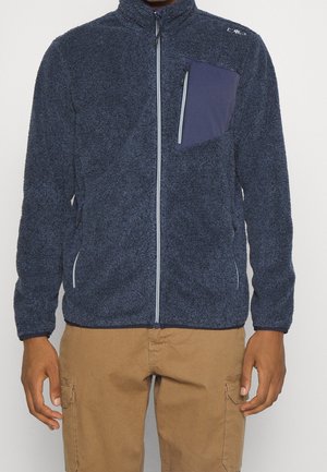 Marineblaue Fleecejacke mit Reißverschluss und kontrastierender Reißverschlusstasche auf der Brust, getragen mit hellbraunen Cargohosen.