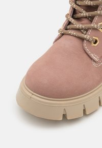 Rosa semsk støvlett med en beige tykk såle, som har brune snører og gullfargede maljer. Teksturert overflatedetalj synlig.