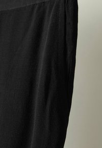 Zwarte stoffen kleding met een gestructureerd oppervlak. Heeft een eenvoudig ontwerp, geplooid detail langs de zijkant en een rechte snit.