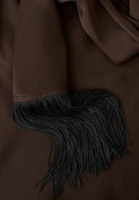 Tissu marron avec une extrémité de manche comportant de longues franges torsadées noires reposant sur le même fond en tissu marron.