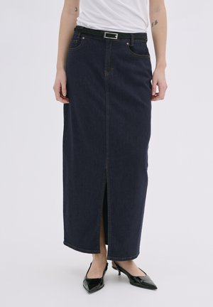 Gonna maxi in denim blu scuro con uno spacco frontale, caratterizzata da cuciture a contrasto e una cintura nera con fibbia argentata, abbinata a tacchi neri.