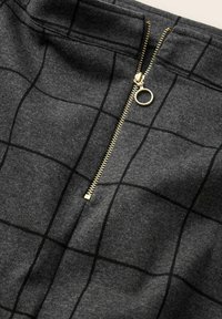 Mörkgrått tyg med svart rutmönster och en delvis öppnad guldfärgad dragkedja med runt dragare.