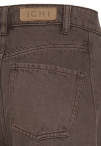 Baglomme på brune denimjeans med synlige syninger og en beige læderlabel med teksten "ICHI" på linningen.