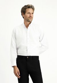 Biała koszula z długim rękawem, z kołnierzykiem, w połączeniu z czarnymi spodniami; gładki materiał; klasyczny krój z zapięciem na guziki z przodu i przy mankietach.