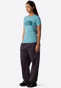 Turquoise short-sleeve t-shirt with black logo on the front, paired with loose-fitting dark gray sweatpants and black footwear.