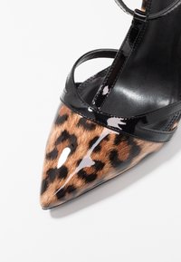 Tacchi alti in pelle verniciata con stampa leopardata, punta affusolata, cinturini neri e interno nero elegante. Presentano una finitura lucida.